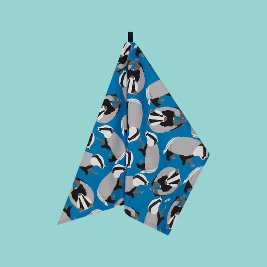 bright Blue Badger Organic Cotton Tea Towel shown handing from corner loop against a pale blue background