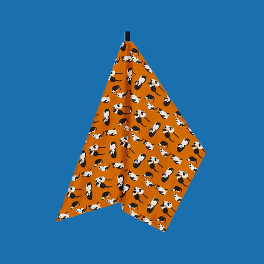 colourful, bright orange organic cotton orange tea towel with illustrations of black and white cats, shown against a plain blue background