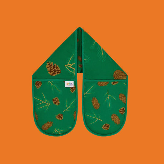 A pair of green oven gloves with an evergreen background and illustrations of Douglas fir cones and spruce sprigs on a orange background.