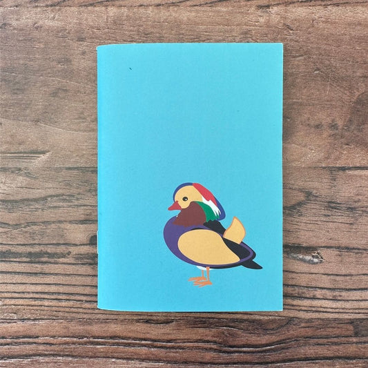 Blue notebook with a colorful duck illustration on a wooden surface
