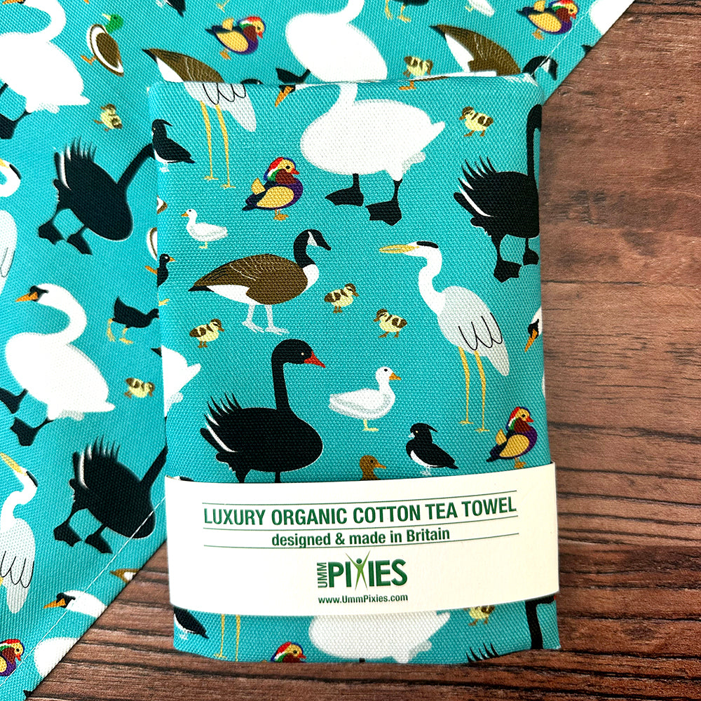 Teal coloured luxury organic cotton tea towel with bird pattern on a wooden surface