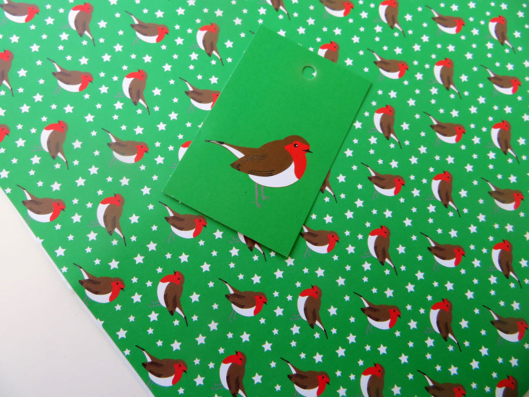 Green wrapping paper with robin design and matching gift tag on a white surface