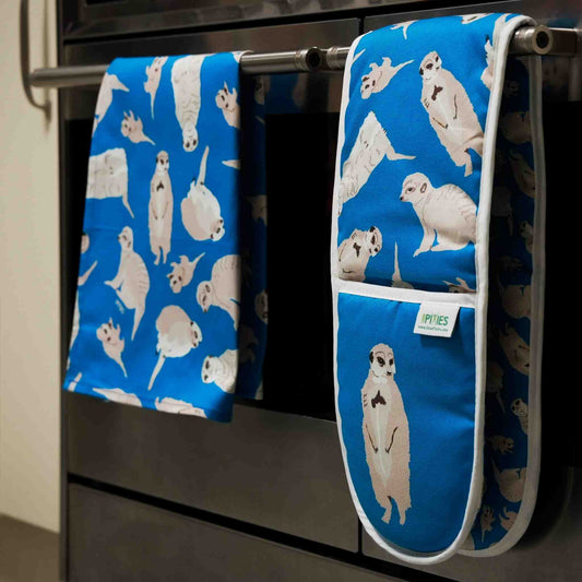 Blue oven mitt and towel with meerkat pattern hanging on a stove.