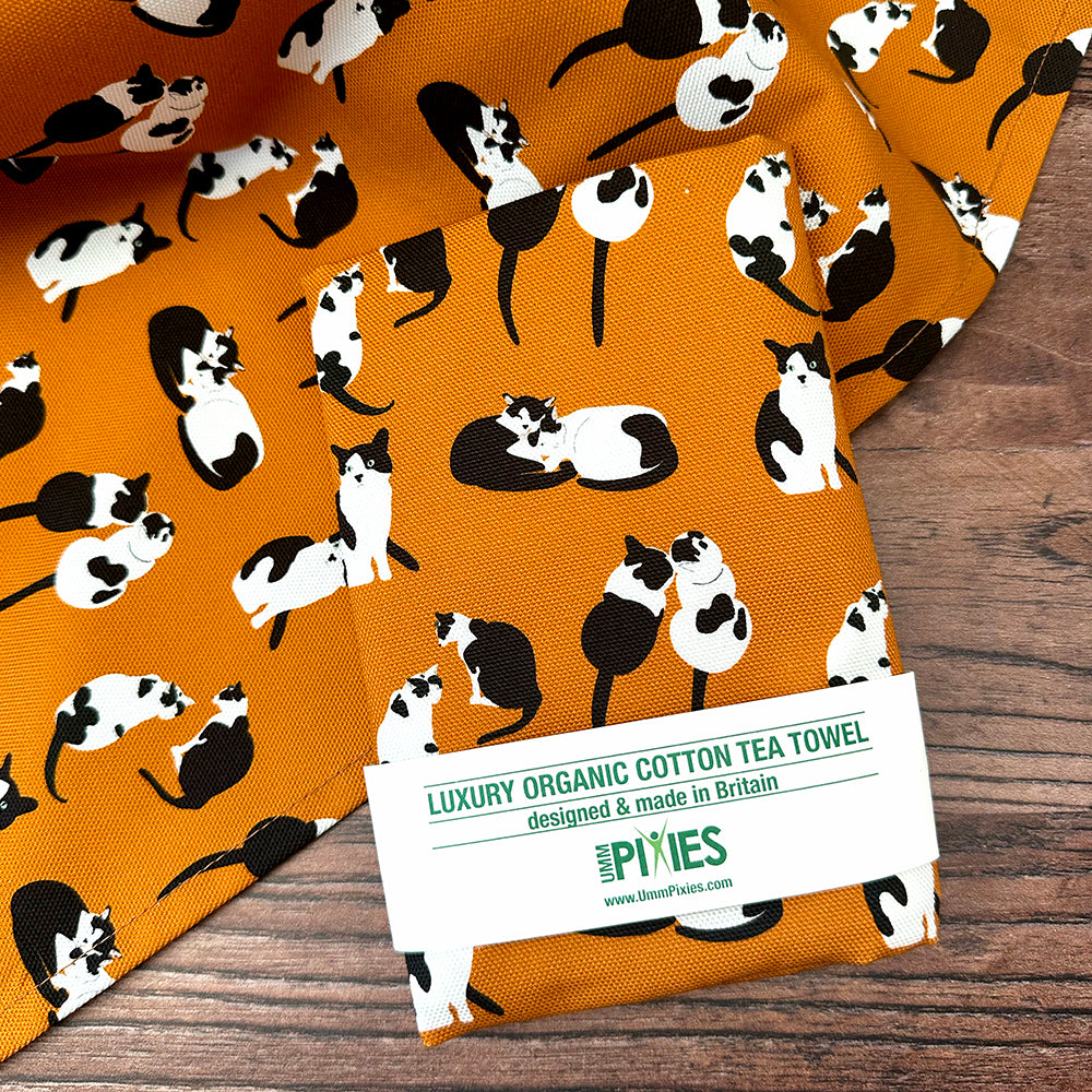 Orange tea towel with black and white cat pattern shown open and in packaging