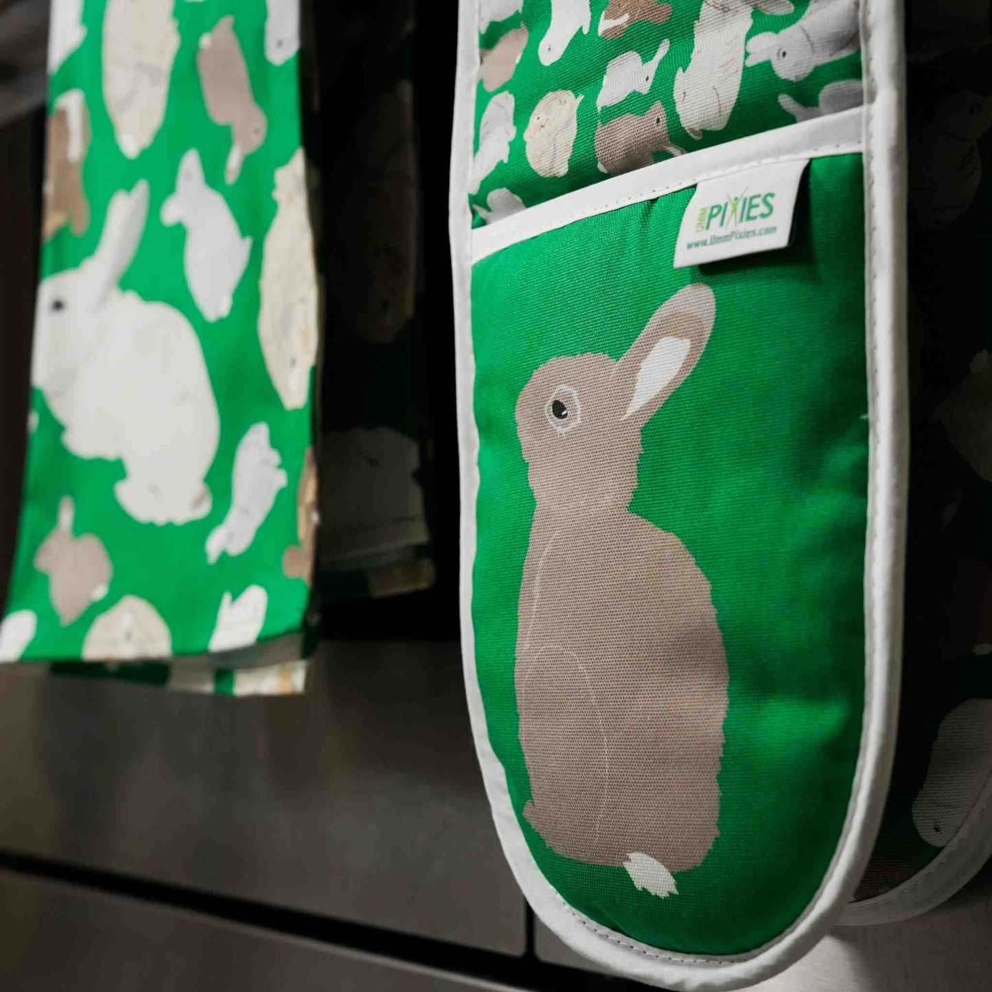 Green oven mitt with rabbit pattern hanging on a stove.