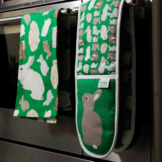 Green oven mitt and towel with rabbit pattern hanging on a stove handle.