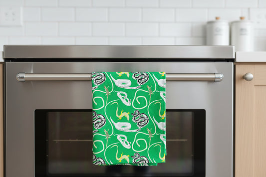 bright green organic cotton tea towel with illustrations of British snakes and lizards shown draped over the handle of an oven door
