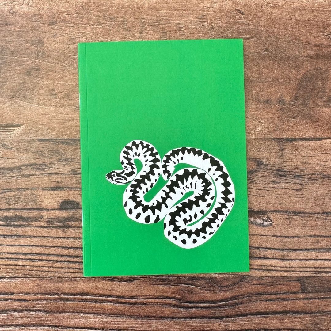 Green notebook with an adder snake illustration on a wooden surface