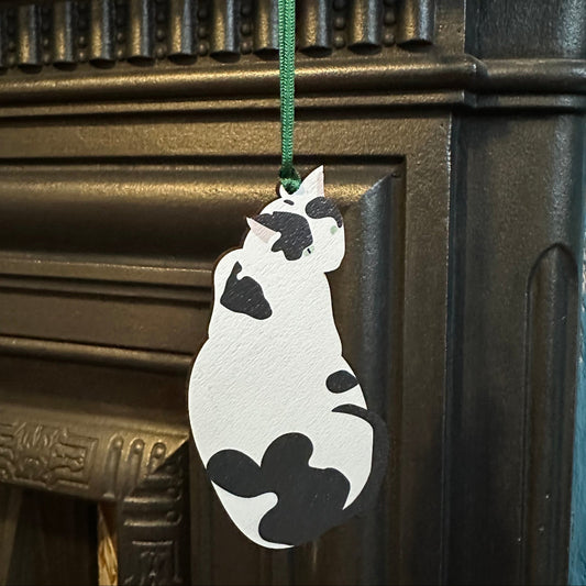 Cat-shaped wooden hanging decoration on a ribbon in front of a fireplace
