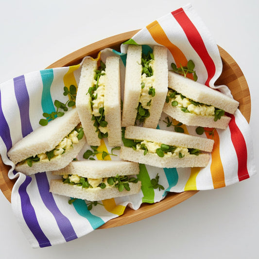 Small sandwiches on a wooden plate with a colorful striped towel underneath