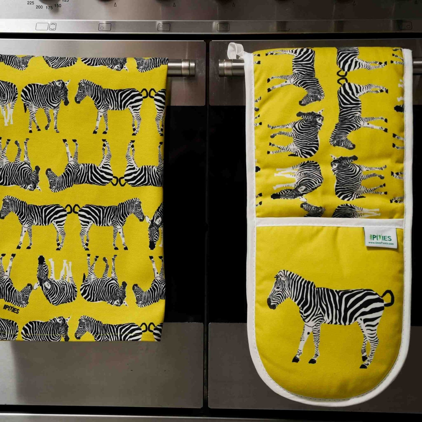 Yellow kitchen towel and matching oven gloves with zebra pattern on a kitchen stove.