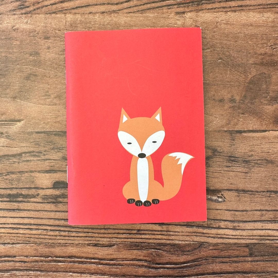 Red notebook with a fox illustration on a wooden surface