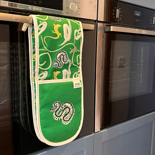 A green oven mitt with a white border and a snake pattern, hanging from the handle of a black Bosch oven in a kitchen setting.