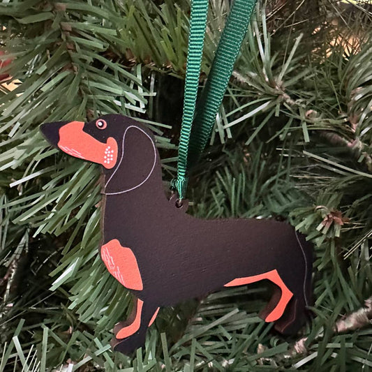 Dog-shaped Christmas ornament on a green ribbon against a pine tree background