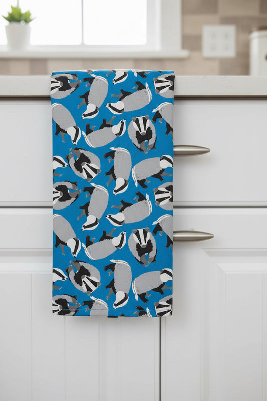Bright blue badger design tea towel shown in a kitchen hanging over the edge of a cabinet