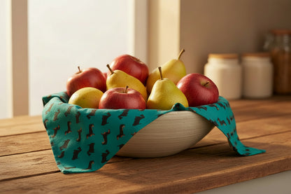 Petrol blue dogs design organic cotton tea towel shown lining a bowl filled with fruit 