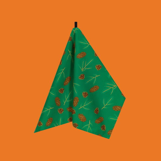 fir and spruce cones and sprigs illustrations on a bright cheerful green organic cotton tea towel shown hanging against a bright orange background