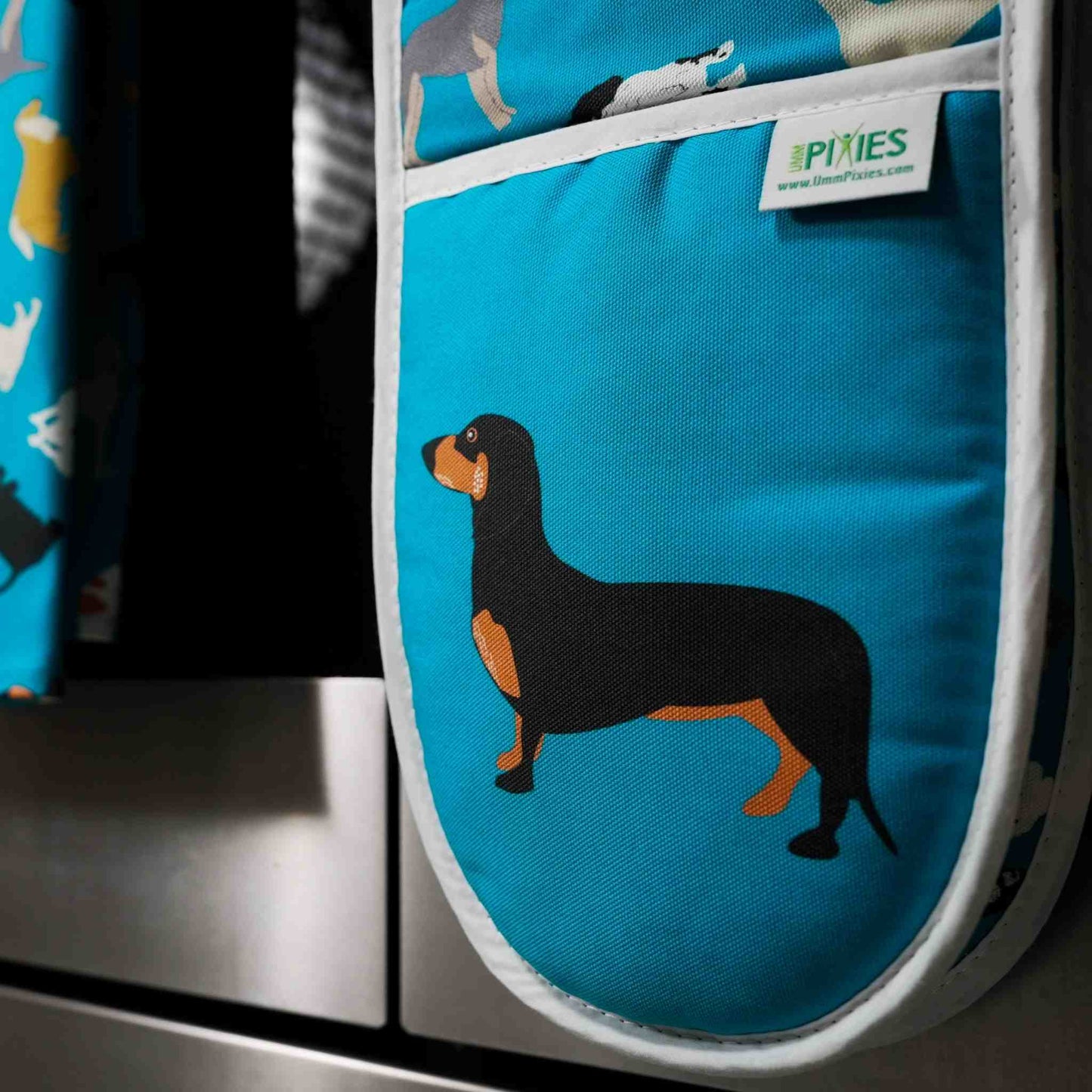 Blue oven mitt with dachshund design hanging on a stove handle