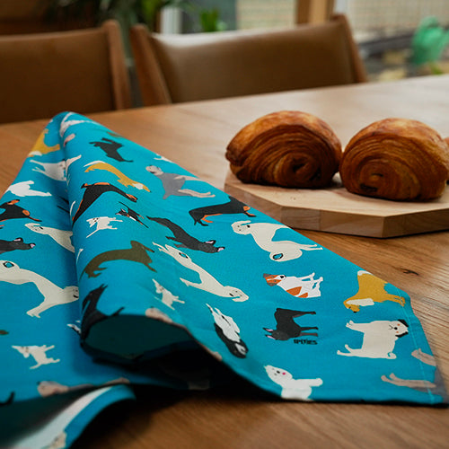 Blue tea towel with dog pattern on a wooden table with croissants.