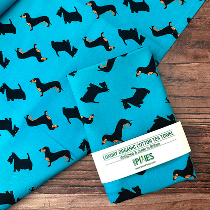organic cotton petrol blue dogtooth dogs tea towel featuring daschund, Scottish terrier and black and white rescue dog shown in UmmPixies bran packaging