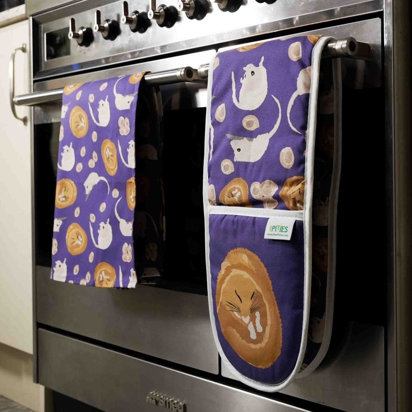 Purple Oven mitt and matching tea towel with sleeping dormouse design hanging on a stove in a kitchen.