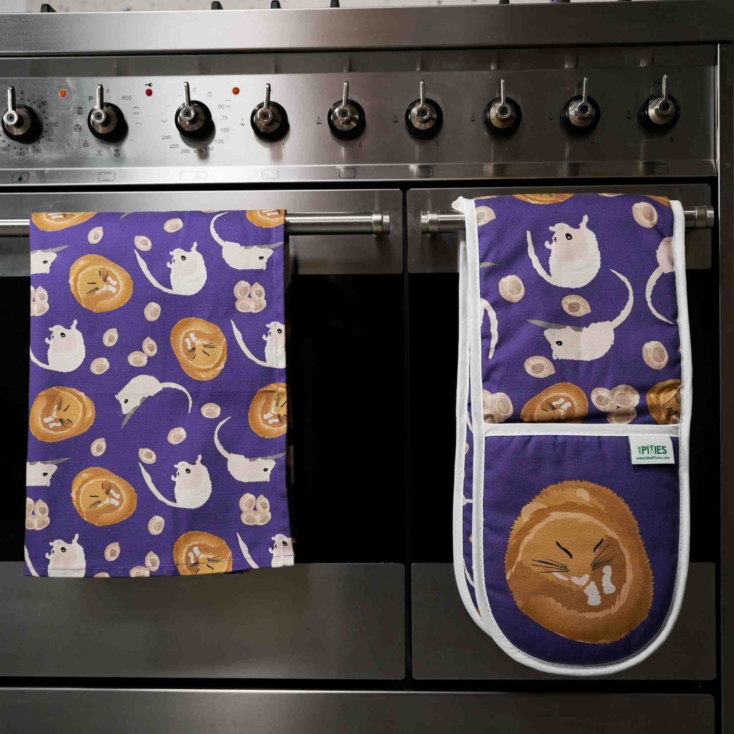purple cotton kitchen towels and matching oven gloves with dornouse patterns hanging on a stove.
