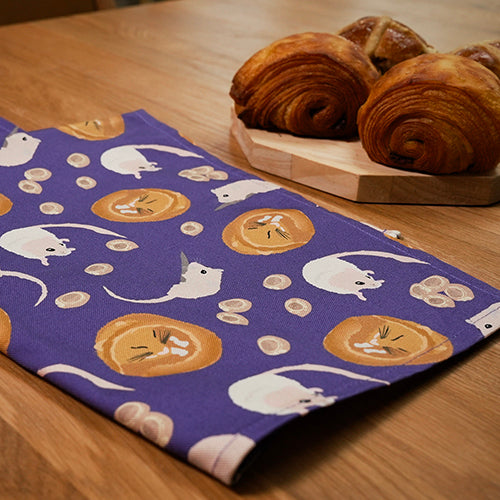 Purple tea towel with dormouse pattern on a wooden table with pastries.