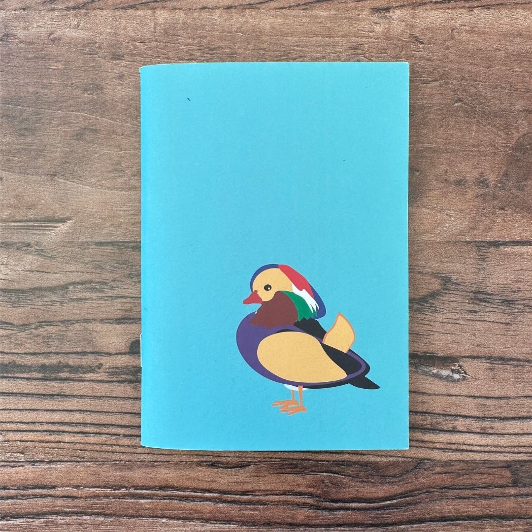 Blue notebook with a colorful duck illustration on a wooden surface
