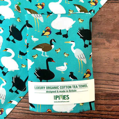 Teal coloured luxury organic cotton tea towel with bird pattern on a wooden surface