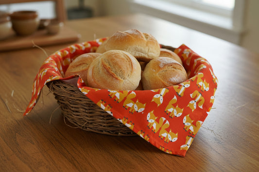 Bright red foxes tea towel shown lining a basket of bread on a wooden table 
