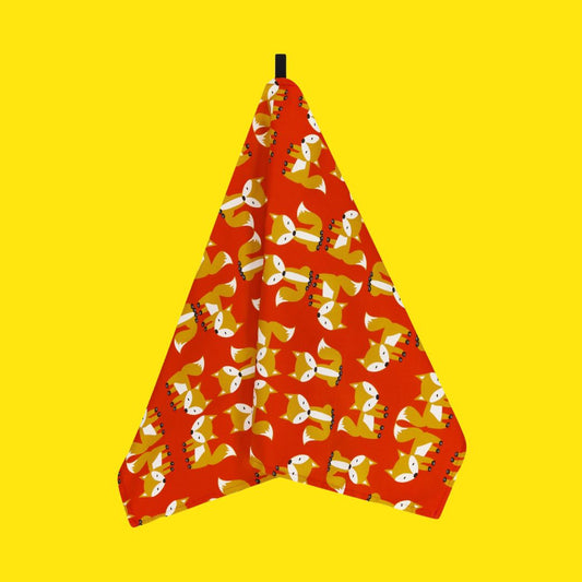 Colourful organic cotton tea towel in a vibrant red featuring the foxes on parade design from UmmPixies. Shown hanging from its own hanging loop against a plain bright yellow background