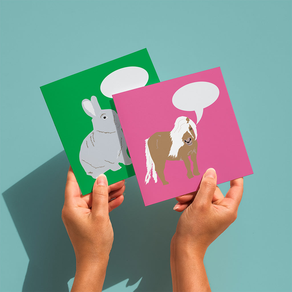 hands holding 2 greetings card, one pink with horse illustration and 1 green with rabbit illustration 