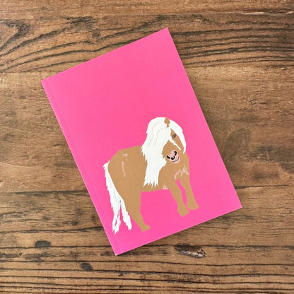 Pink notebook with a horse illustration on a wooden surface
