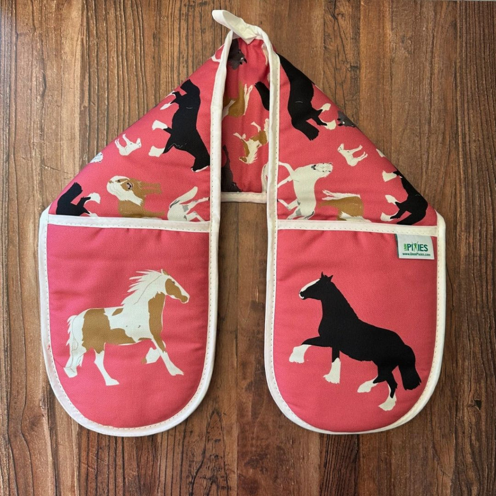 Pair of pink oven mitts with horse designs on a wooden surface