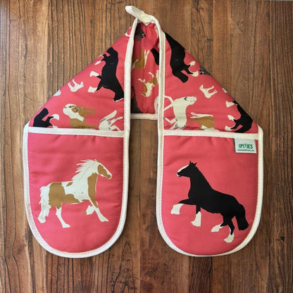 Pair of pink oven mitts with horse designs on a wooden surface