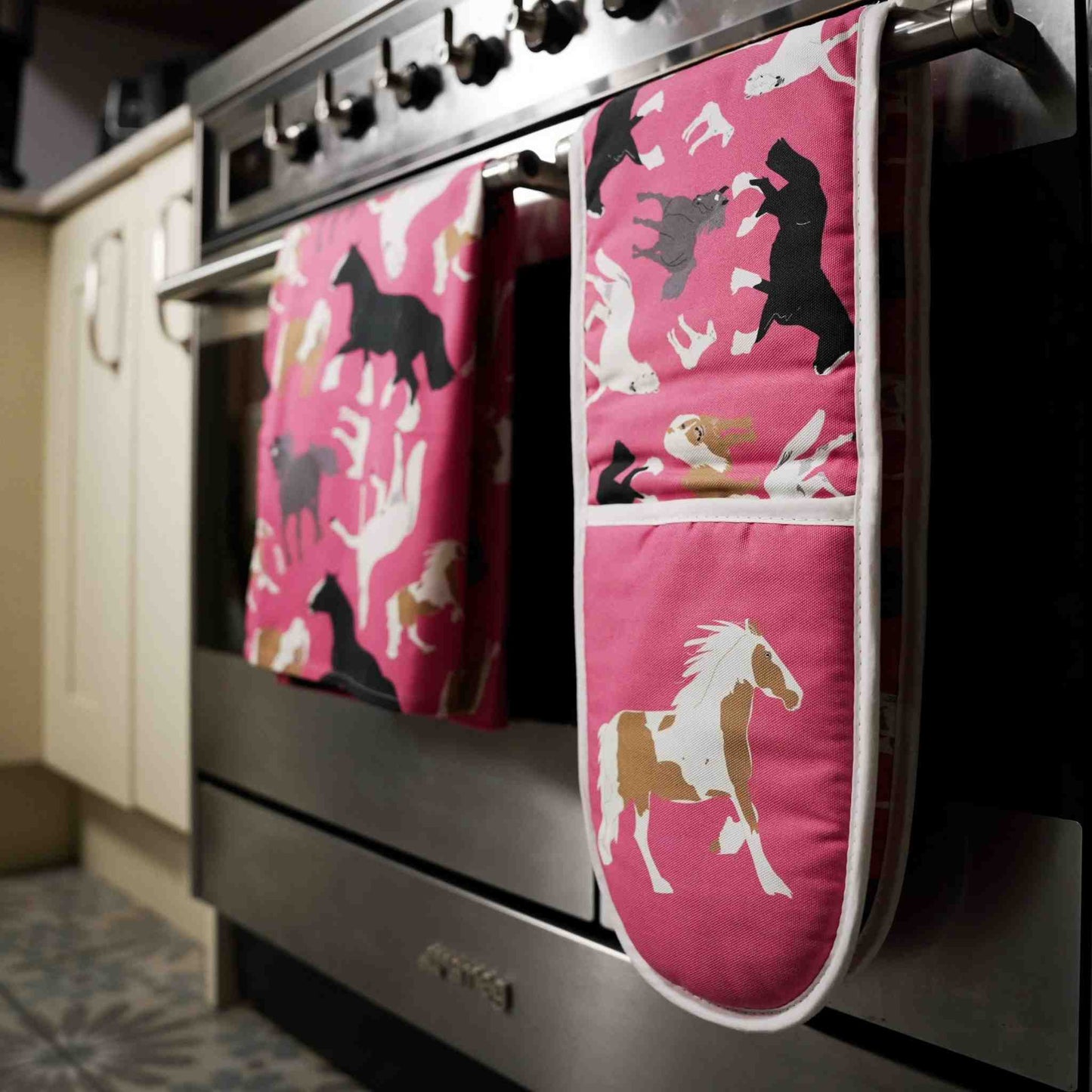 Pink oven mitts with horse pattern hanging on a stove handle
