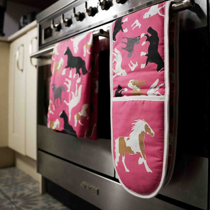 Pink oven mitts with horse pattern hanging on a stove handle