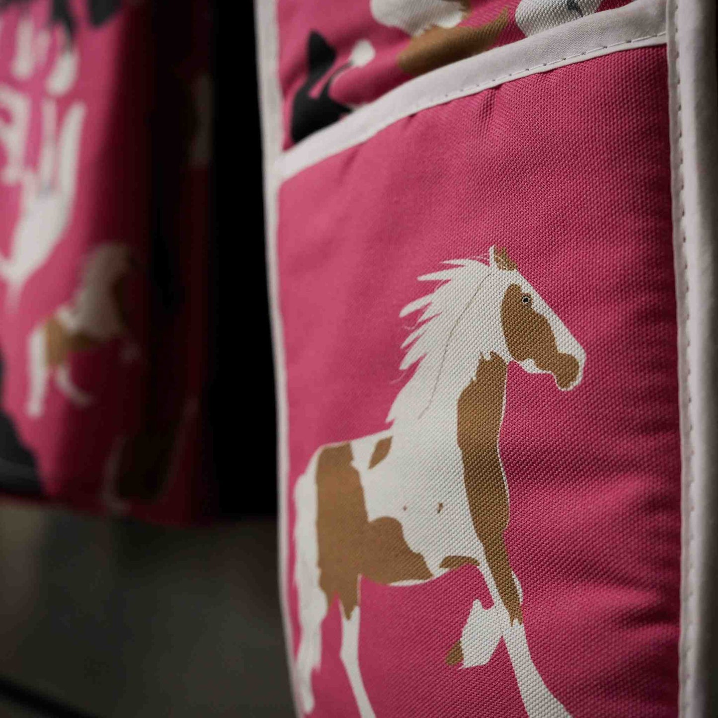 Pink oven gloves with horse illustrations: close up image of them hanging on a stove