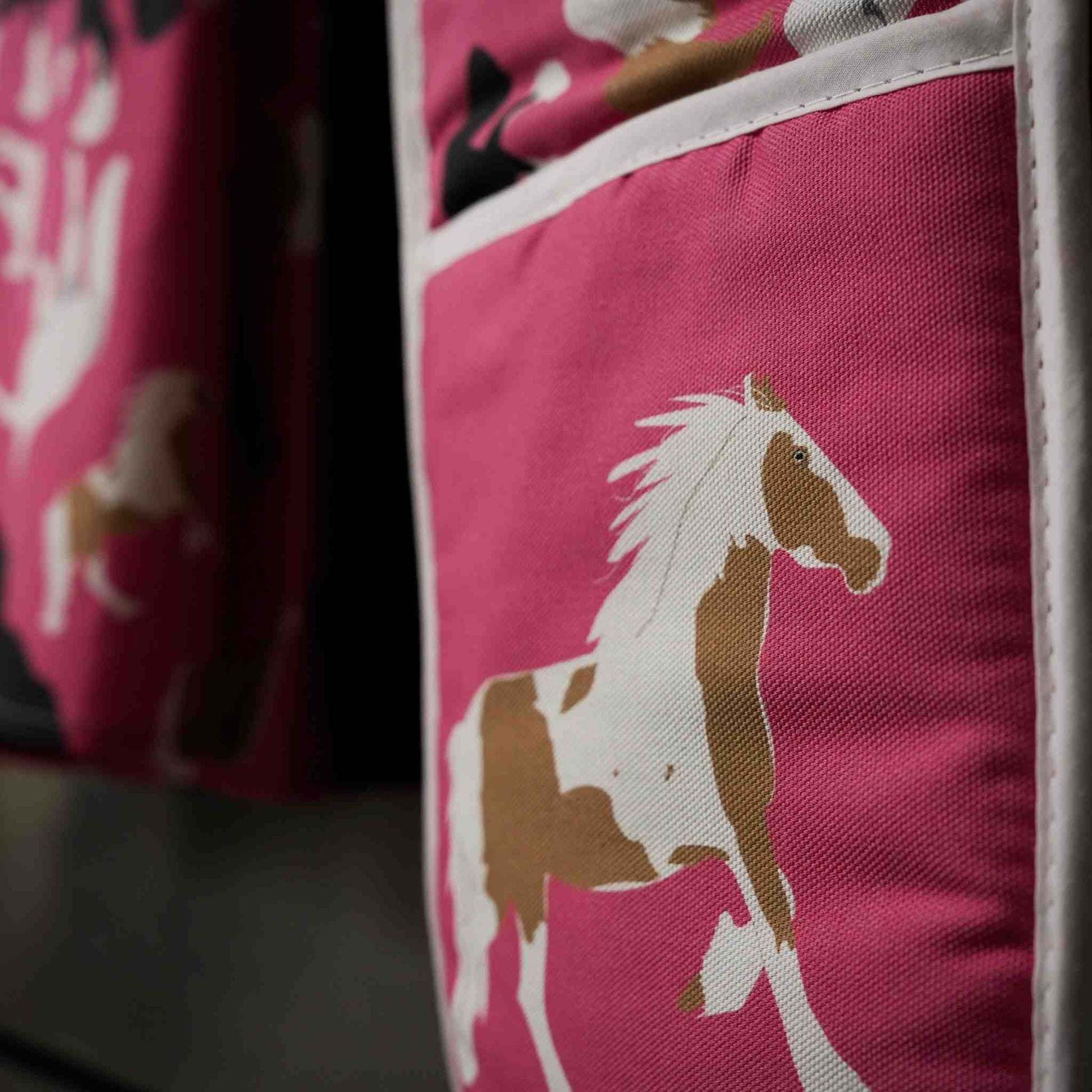 Pink oven gloves with horse illustrations: close up image of them hanging on a stove