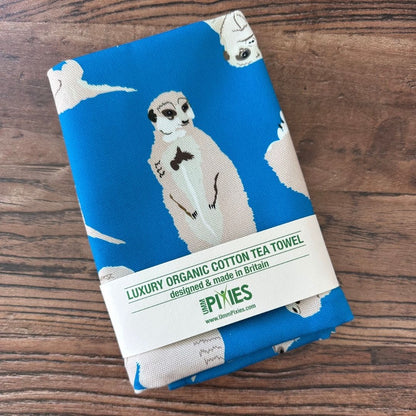 Bright Blue Meerkat design organic cotton tea towel on a wooden table top