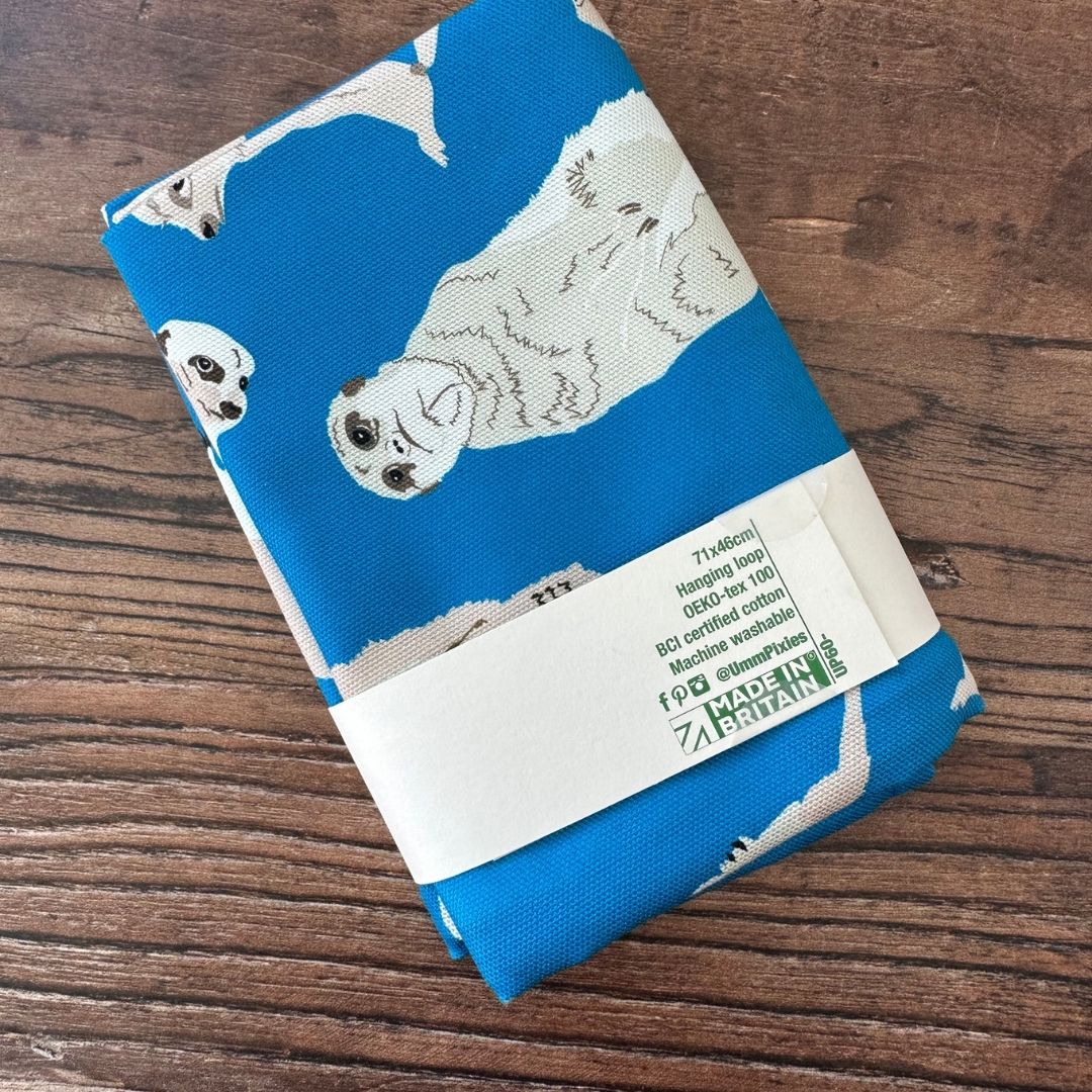 Bright Blue Meerkat design organic cotton tea towel  on a wooden table top