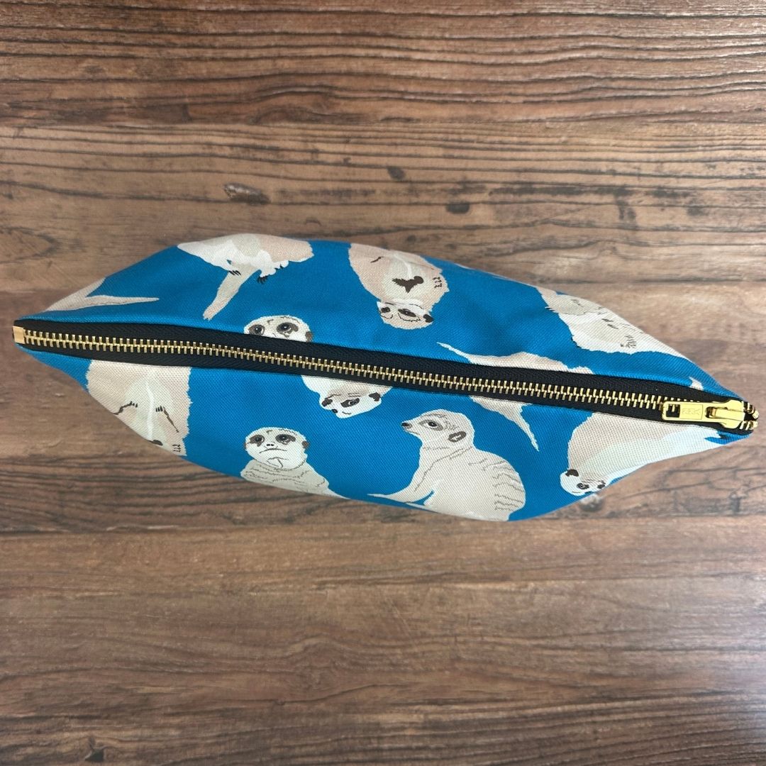 Bright blue Meerkats illustrated really useful bag shown from above with zip closed on a wooden surface