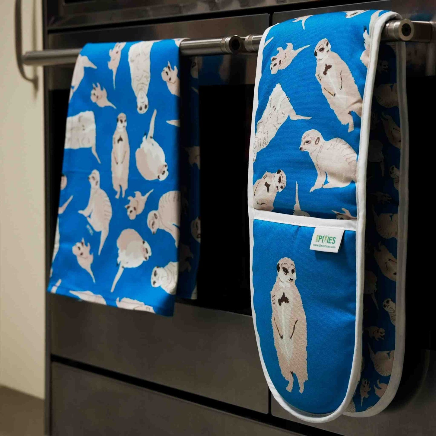 Blue oven mitt and towel with meerkat pattern hanging on a stove.
