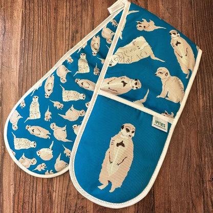 Bright blue cotton oven gloves with meerkat illustrations on a wooden surface
