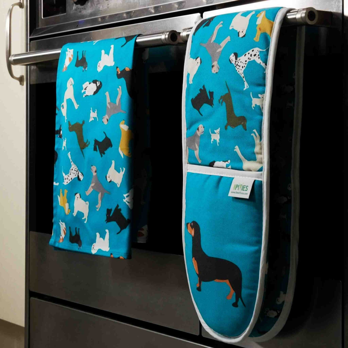 Blue dogs design oven mitts and matching tea towel shown hanging on a stove