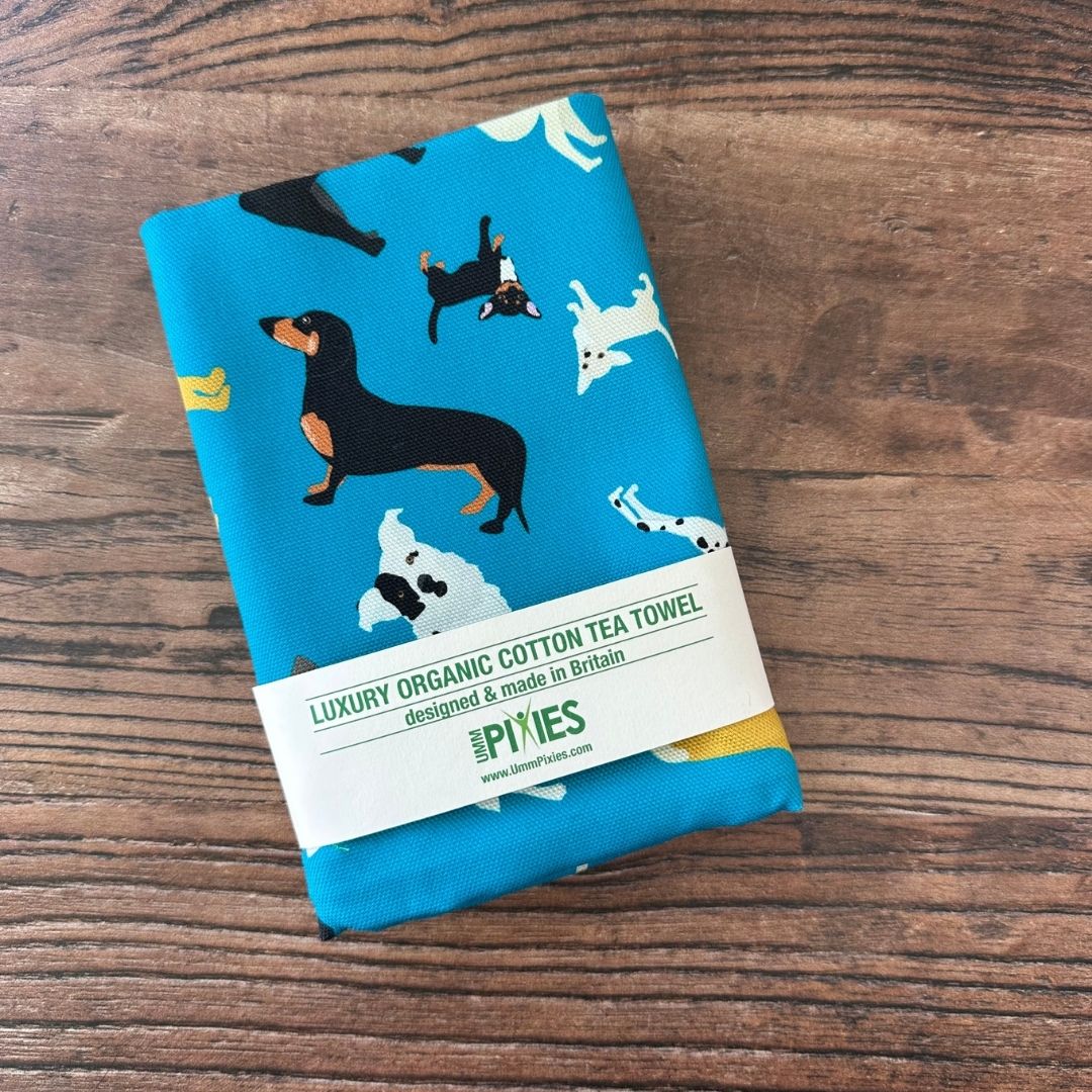 Petrol Blue New Tricks Dogs design organic cotton tea towel shown in orginal packaging on a wooden counter