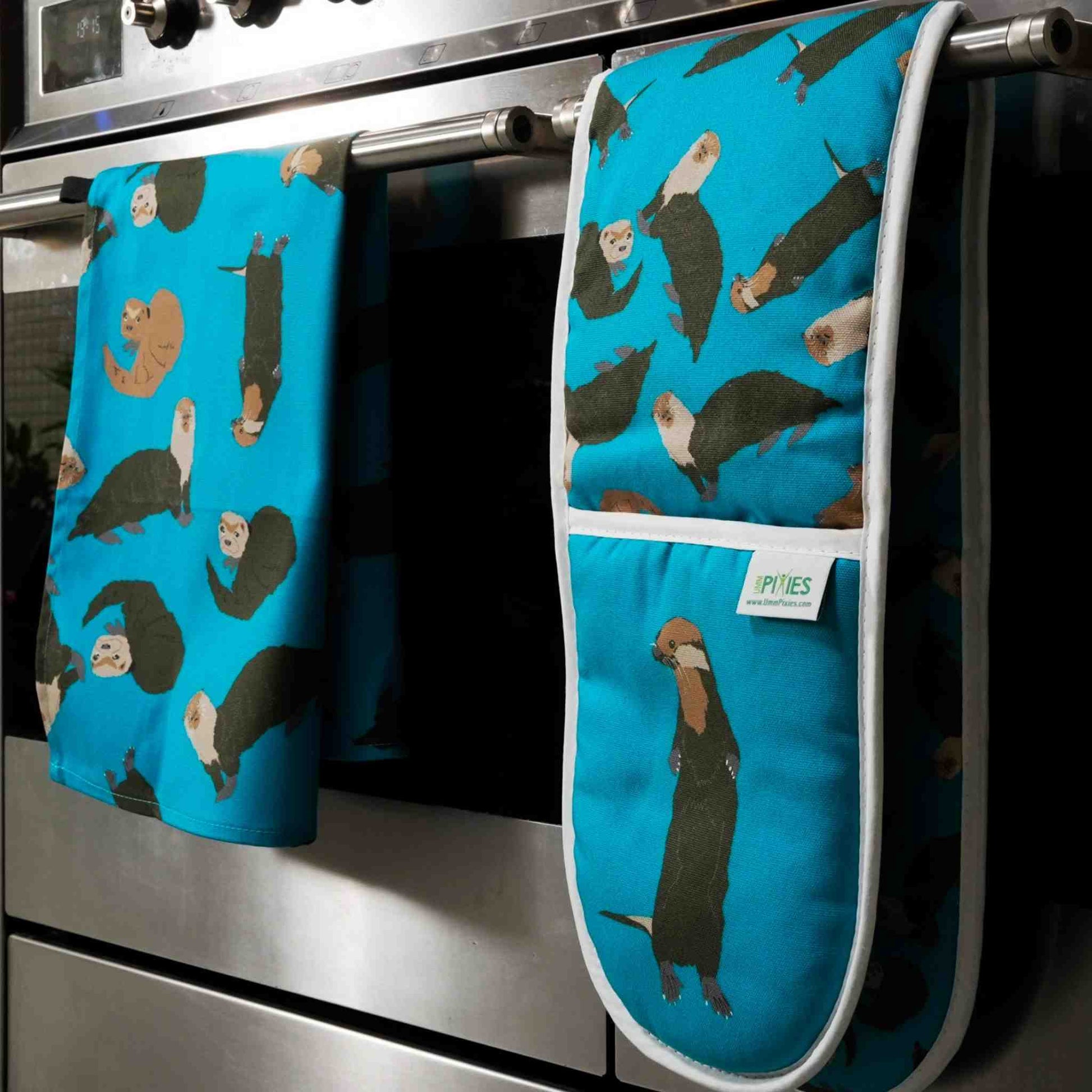 Blue oven mitt and pot holder with otter pattern hanging on a stove.