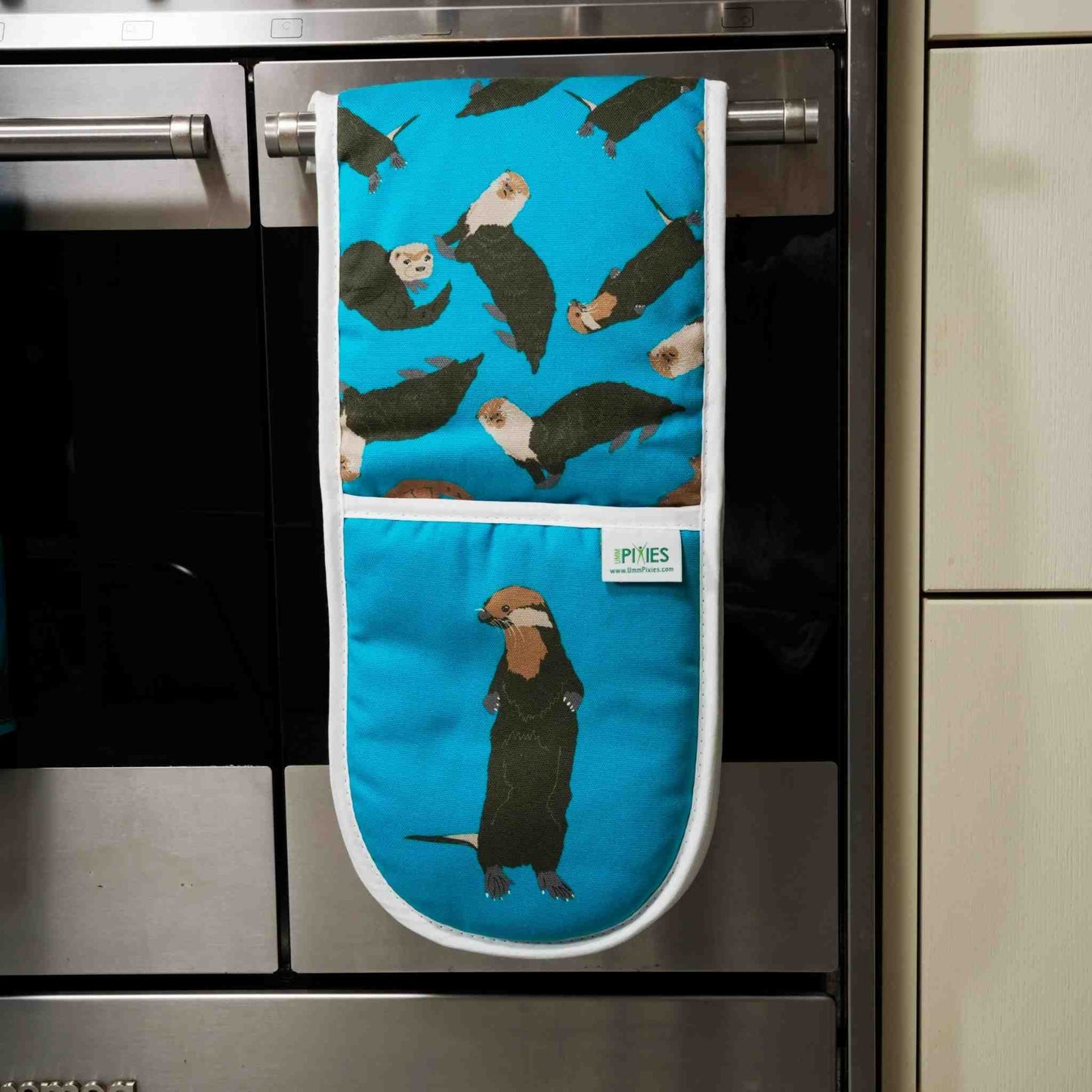 Blue oven mitt with otter pattern hanging on a kitchen appliance.