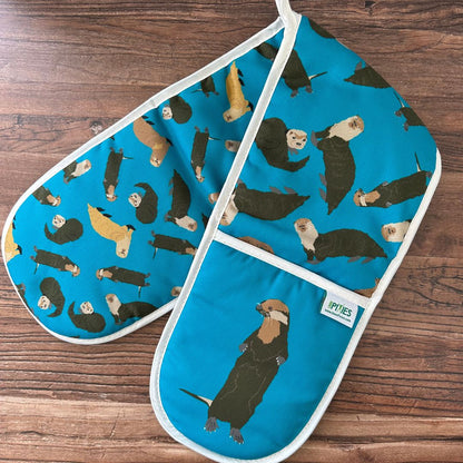 Pair of oven mitts with otter pattern on a wooden surface