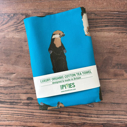 Petrol blue otters design organic cotton tea towel shown in packaging on wooden table
